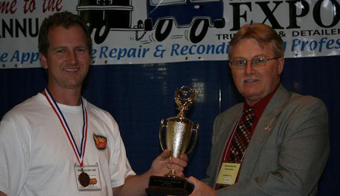 Two men holding a trophy in front of a truck.