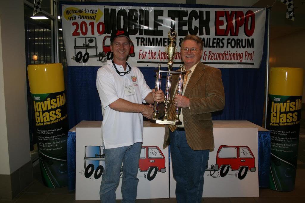 Two men holding trophies in front of a sign.