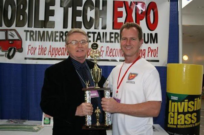 Two men holding a trophy in front of a sign.