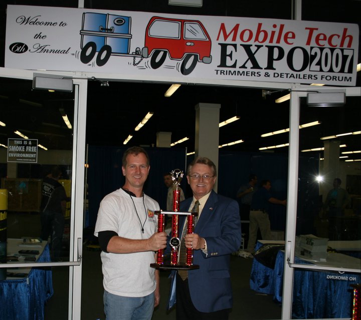 Two men holding a trophy in front of a sign.