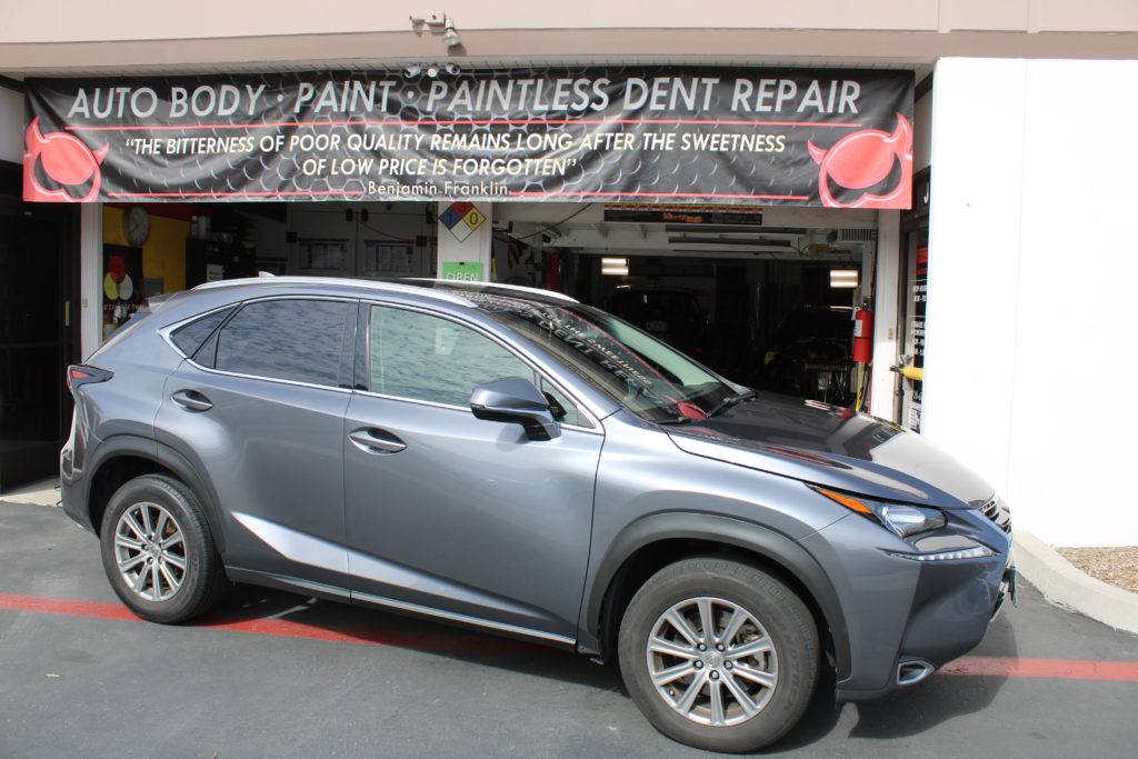 A car parked in front of a dent repair shop.