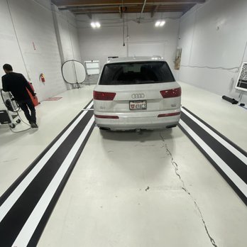 A man is walking in the garage with his car.